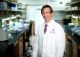 Researcher in lab coat smiling while looking forward.