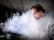 Researcher peering into drum of dry ice as vapor swirls around him.