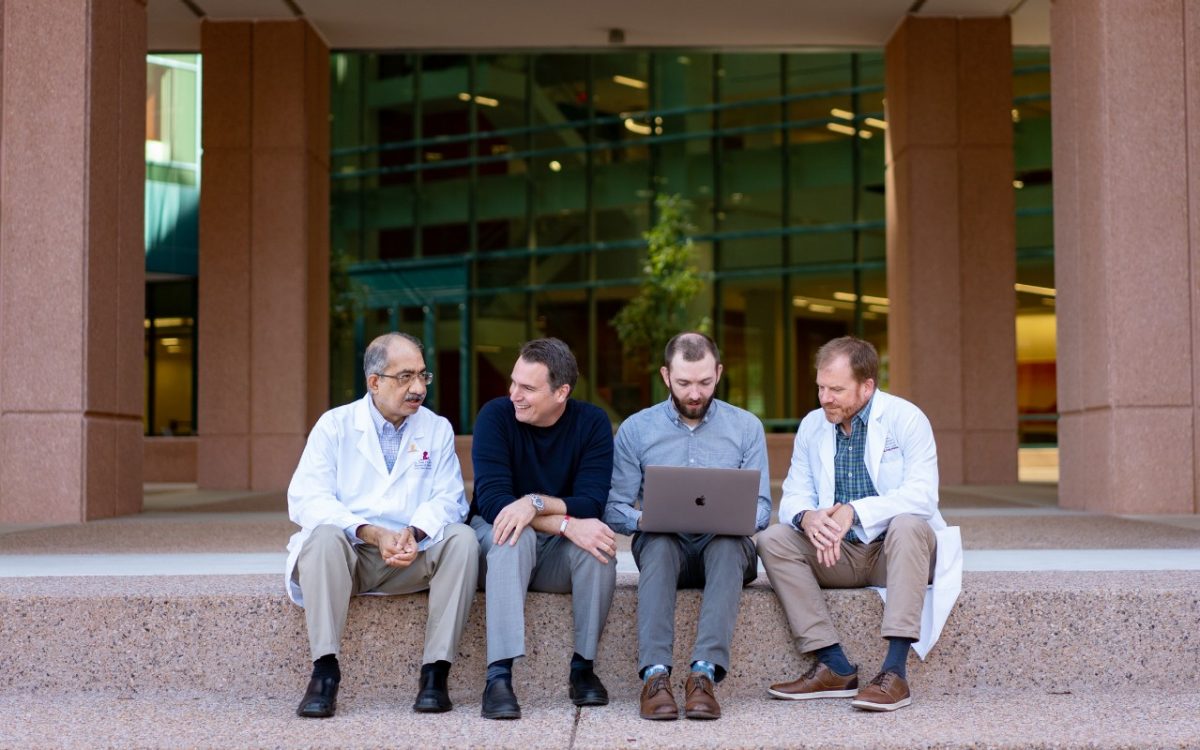 Four researchers sitting on stairs in front of a building talking.