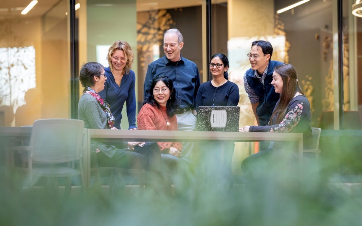 A group of scientists are laughing at someone's remark as they sit around a table