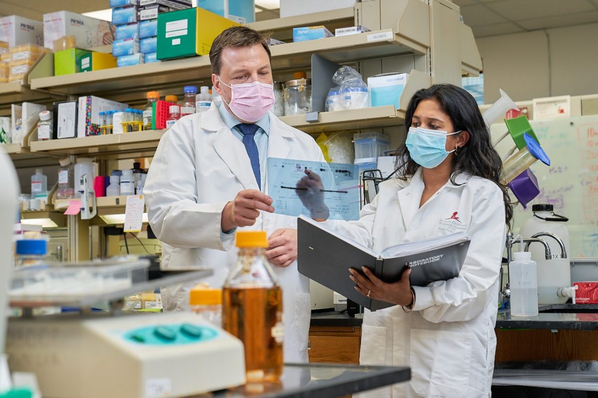 Two reasearchers wearing masks and labcoats looking at documents in the lab.