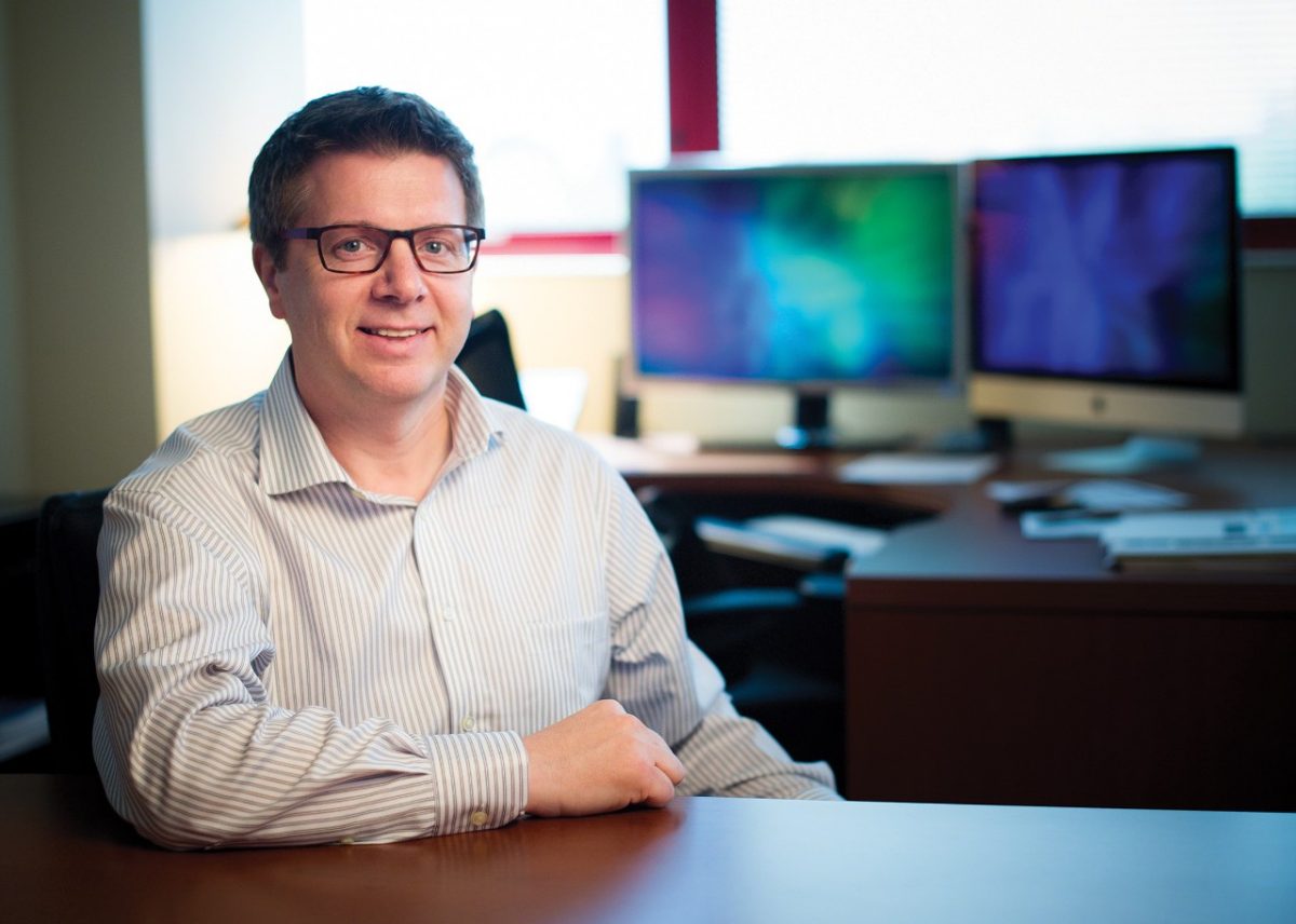 Scientist J. Paul Taylor sitting at his desk with computer screens in the background