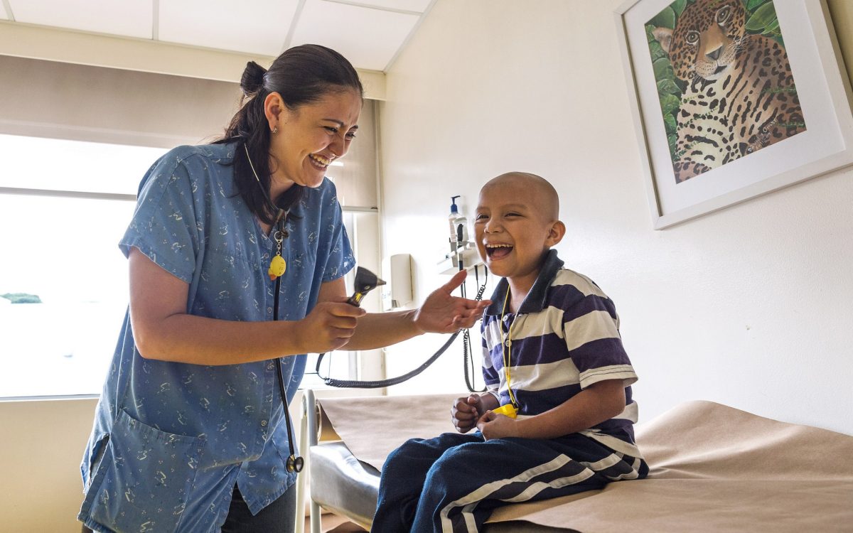 In a Guatemalan hospital room, a nurse is laughing with a boy who is being treated for cancer