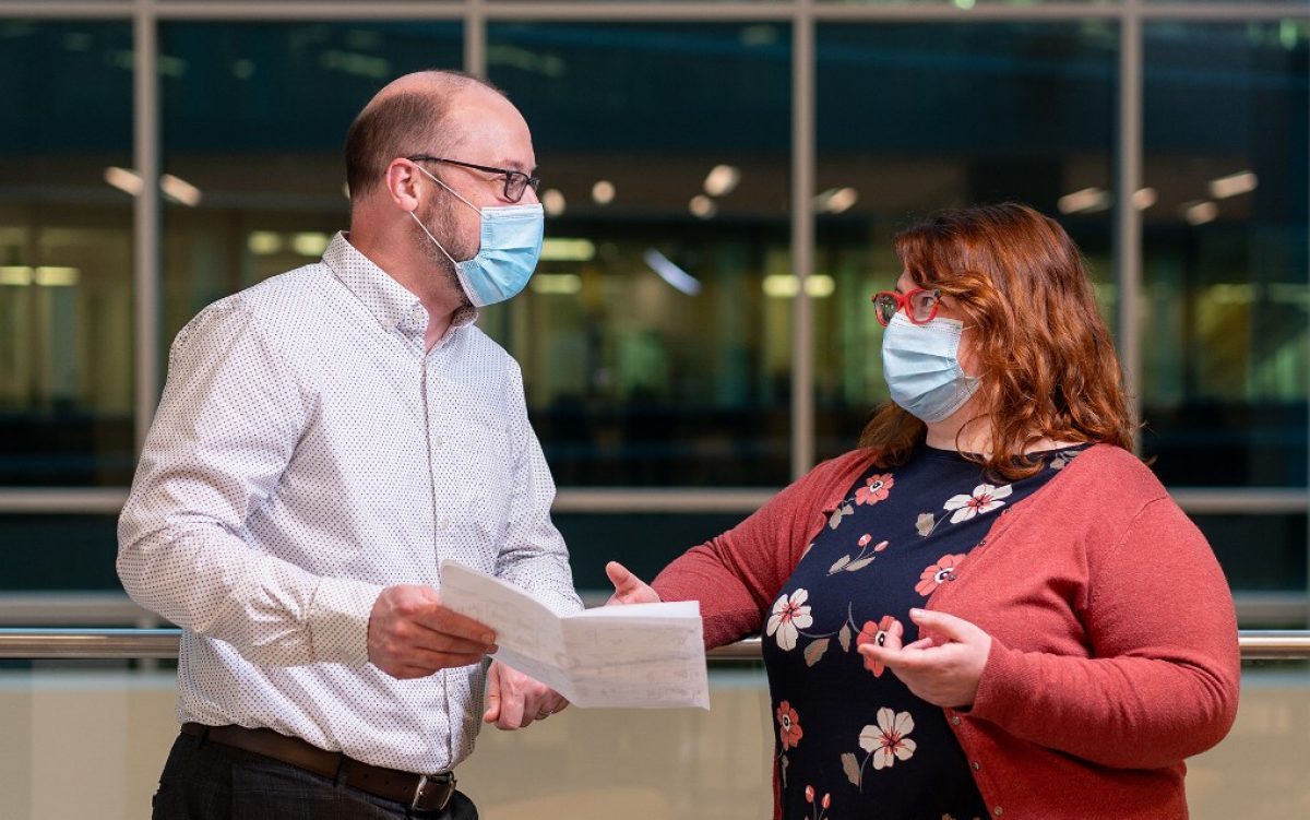 Two scientists, Ben Youngblood and Ardie Moustaki, look at a document. They are wearing surgical masks.