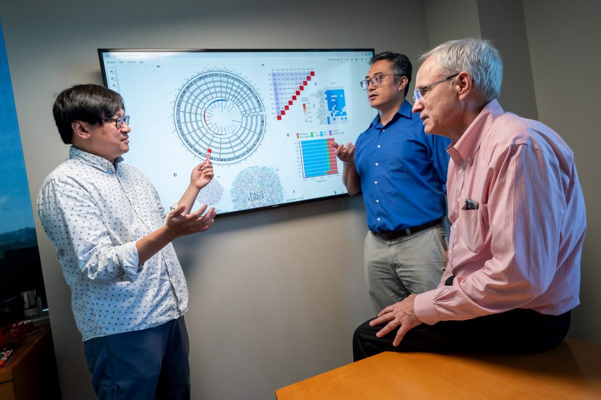 three men standing in front of computer screen