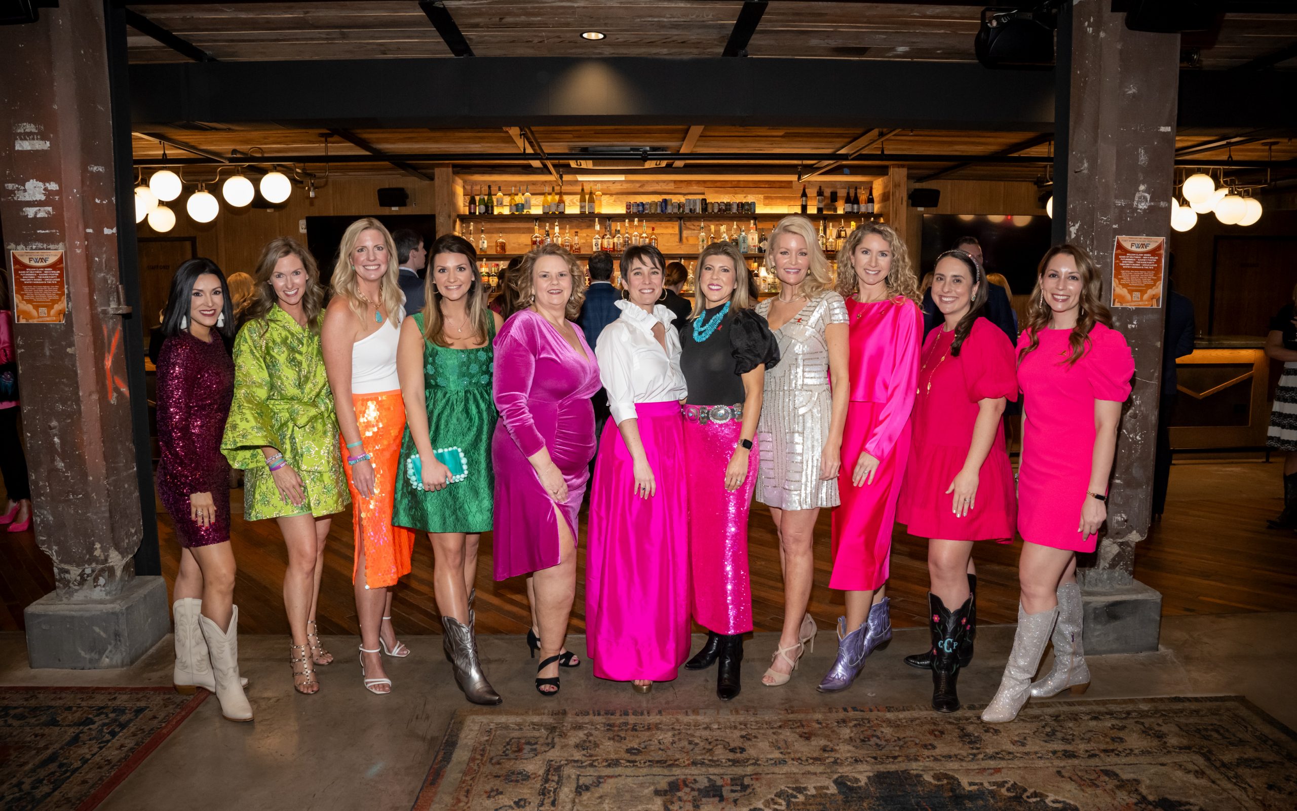 St. Jude Celebration at Sundown attendees smile and pose wearing bright pink, green and orange dresses.