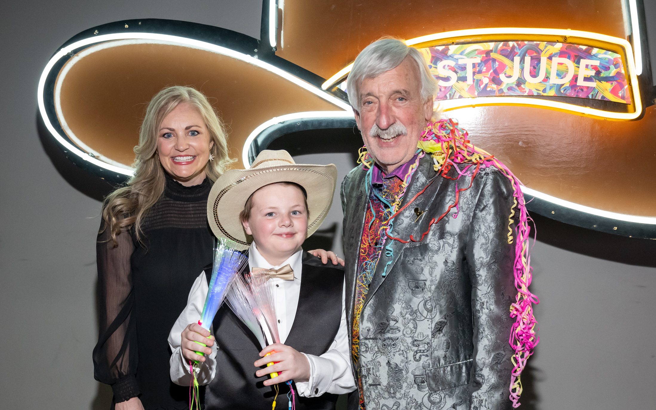St. Jude Celebration at Sundown attendees smile and pose in front of a cowboy hat made of neon lights. 