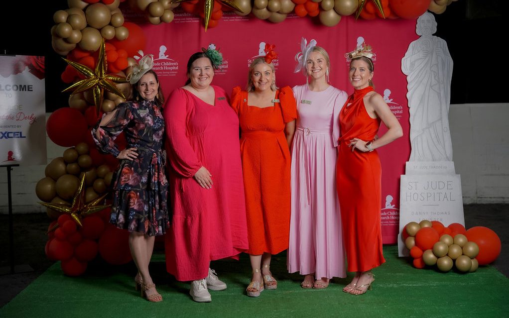 A Day at the Derby attendees pose in long gowns beside a statue of St. Jude. 