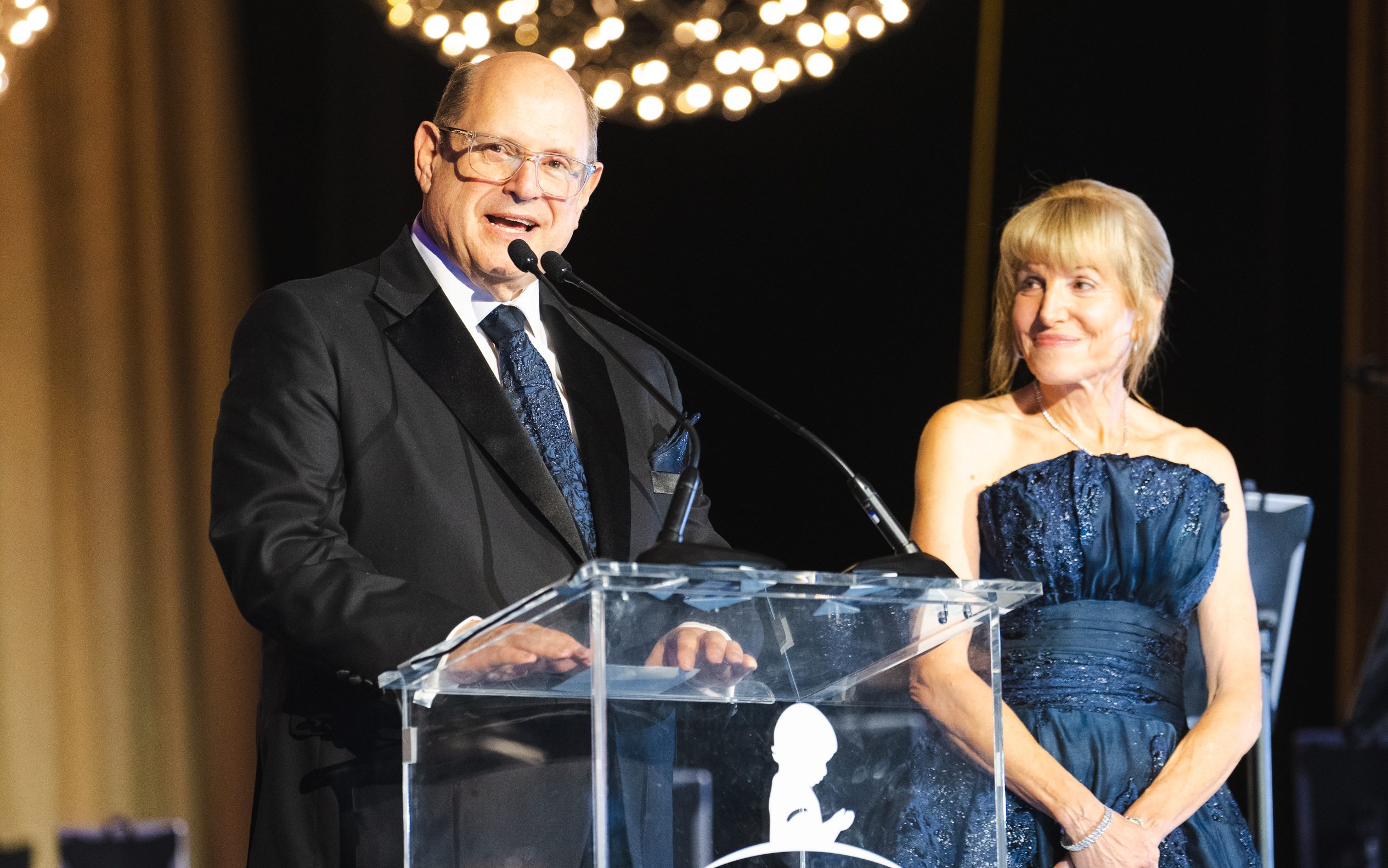 St. Jude Evening of Hope committee chairs Mickey and Lee Segal stand at a podium on stage. 