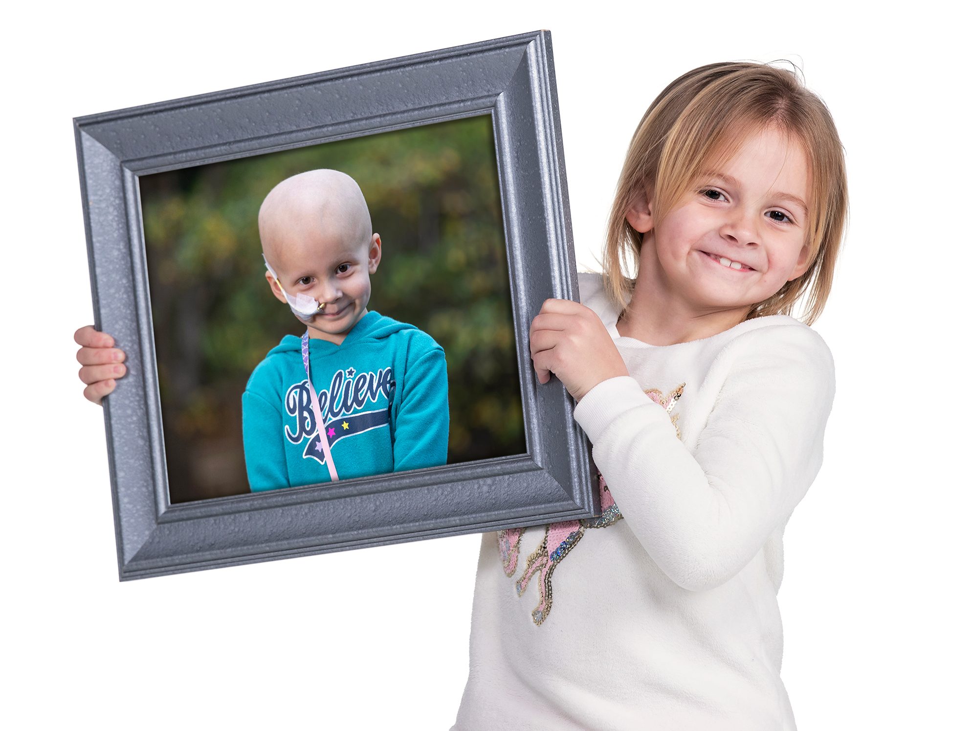 Patient Josie smiles while holding a photo of herself from when she was receiving treatment at St. Jude. 